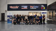 Large group of employees posing together in front of automotive service business with company logos on signage