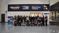 Large group of employees posing together in front of automotive service business with company logos on signage