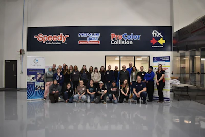Large group of employees posing together in front of automotive service business with company logos on signage