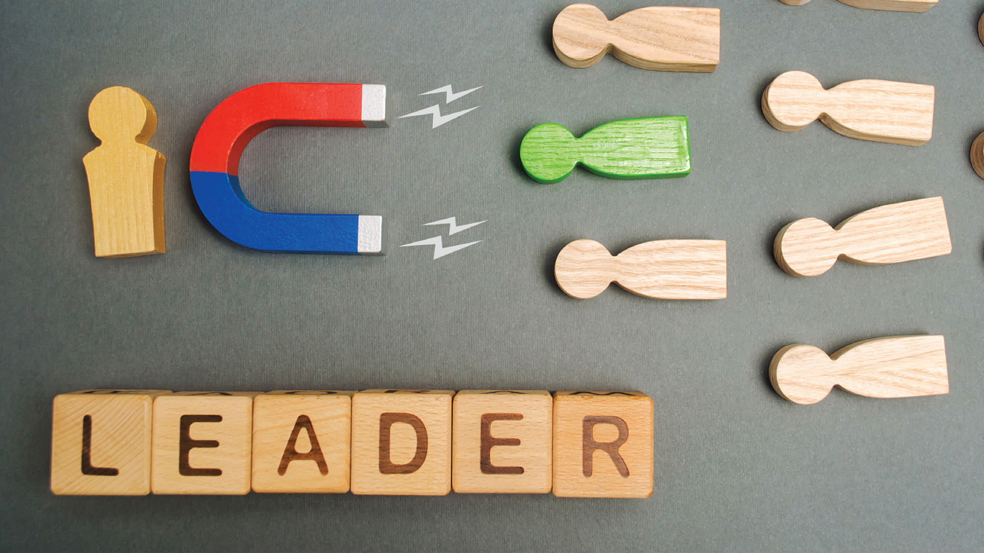 Wooden figures with magnet illustration and LEADER text blocks representing talent attraction and leadership concept