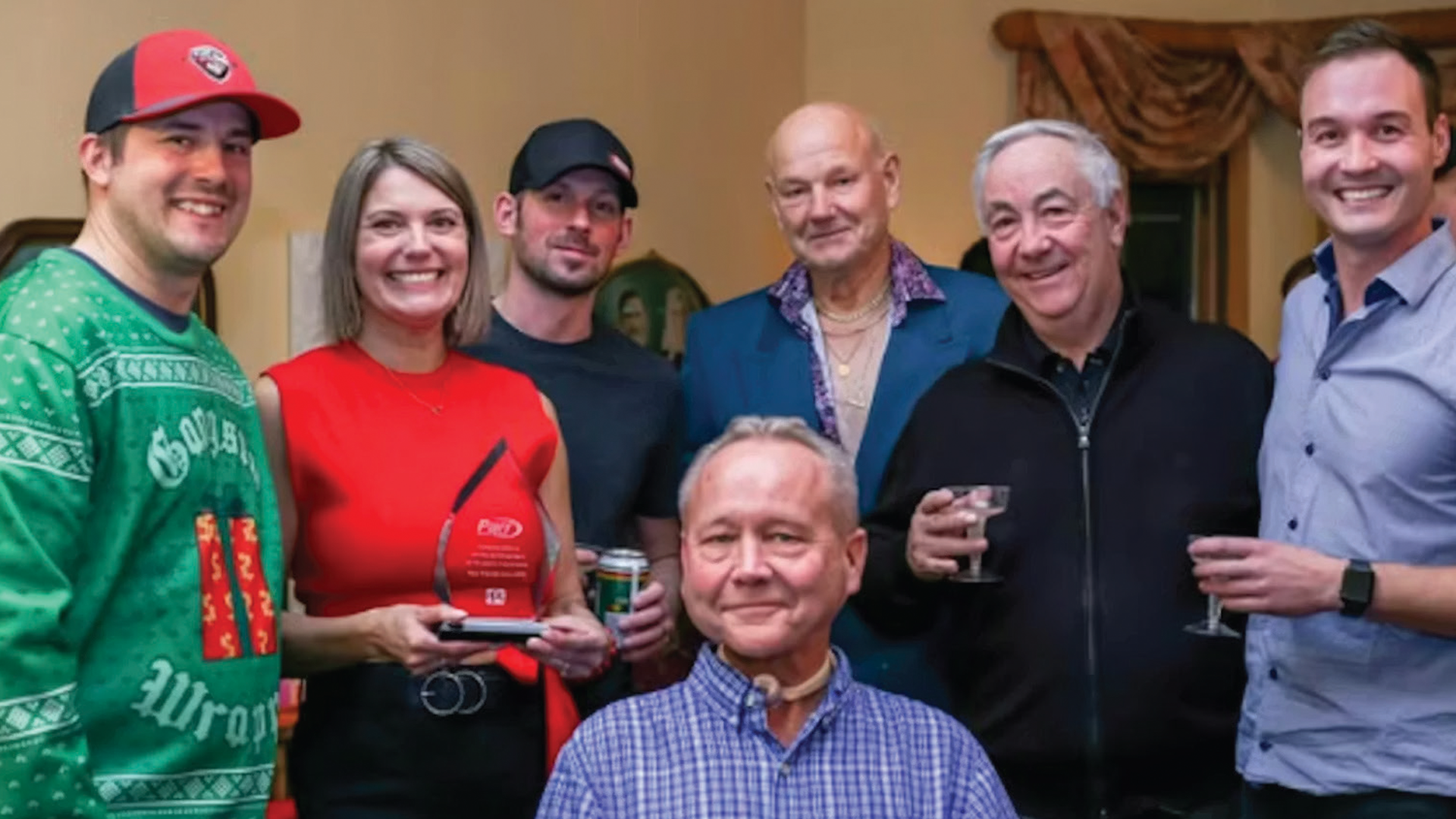 Group of seven people smiling at an indoor gathering, holding drinks and awards