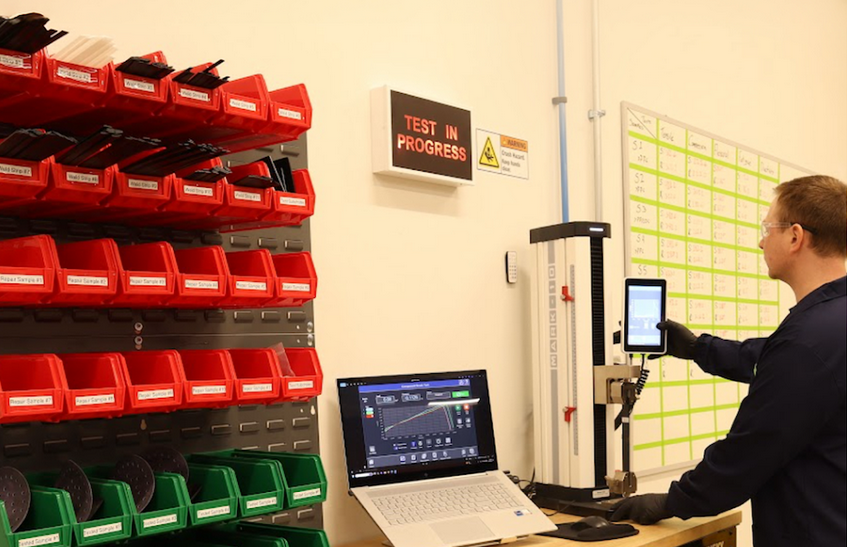 Technician operating testing equipment in industrial workspace with organized red and green storage bins