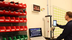 Technician operating testing equipment in industrial workspace with organized red and green storage bins