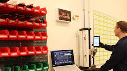 Technician operating testing equipment in industrial workspace with organized red and green storage bins