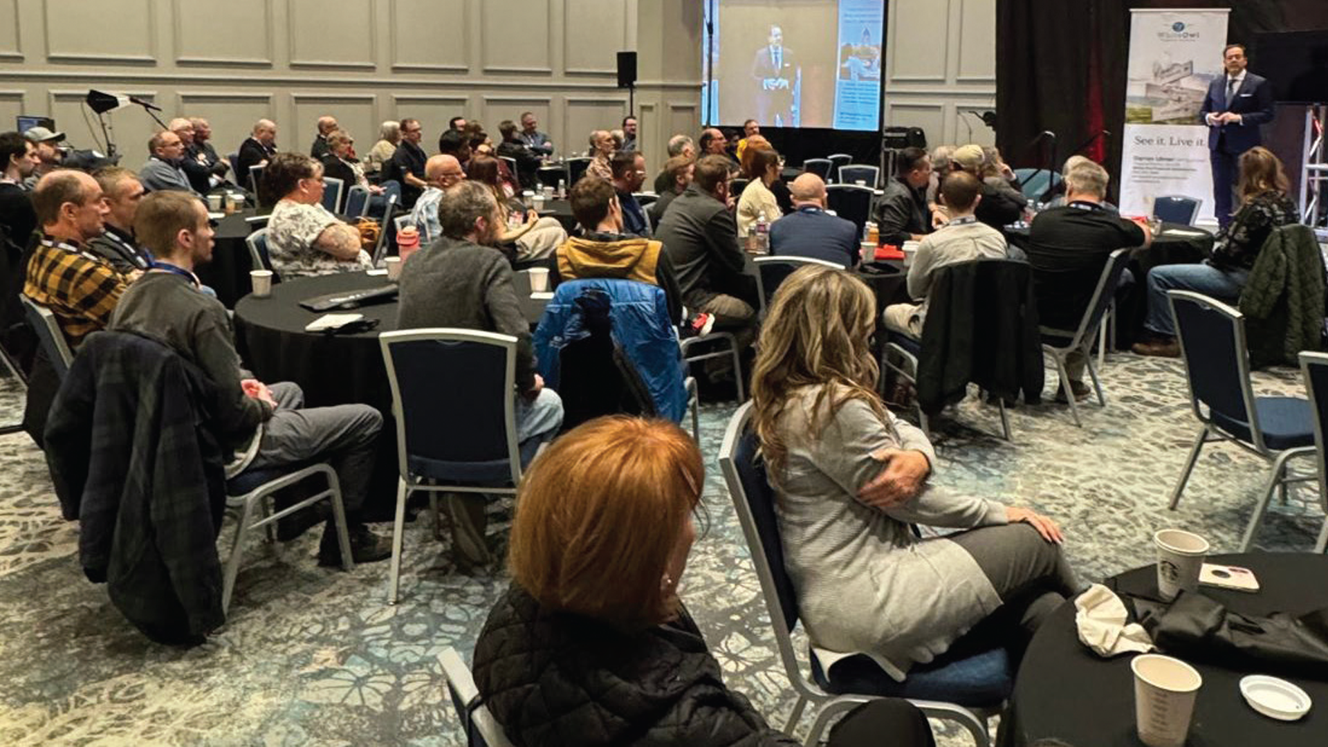 Conference attendees seated at round tables during a business event presentation