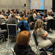 Conference attendees seated at round tables during a business event presentation