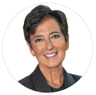 Professional headshot of a woman with short dark hair wearing a black blazer and pearl necklace, smiling against a white background