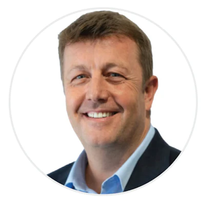 Professional headshot of a smiling middle-aged man wearing a dark blazer and light blue shirt