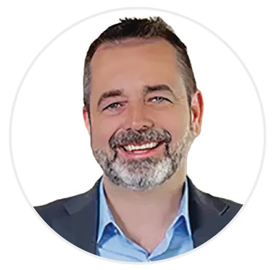 Professional headshot of a bearded man in business casual attire smiling at camera