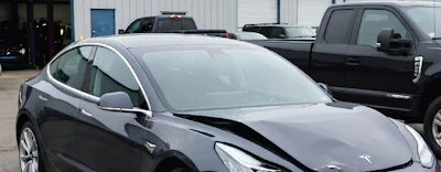 Silver Tesla Model 3 parked in front of a service facility with other vehicles visible