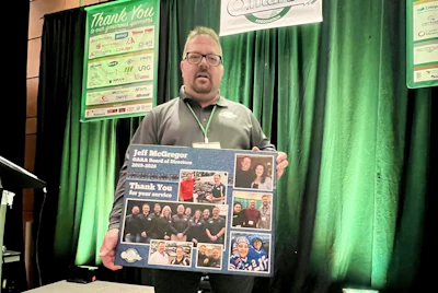 Man holding commemorative poster with photos at event with sponsor banners