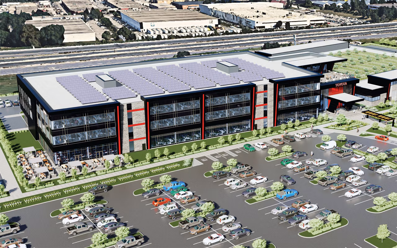 Modern industrial facility with solar roof panels, red and white facade, and landscaped parking lot adjacent to highway