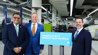 Three business professionals holding blue banner promoting investment in B.C.'s collision repair workforce at industrial facility