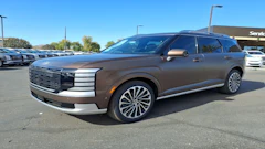 Bronze luxury SUV parked in dealership lot with clear sky and service building visible