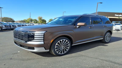 Bronze luxury SUV parked in dealership lot with clear sky and service building visible