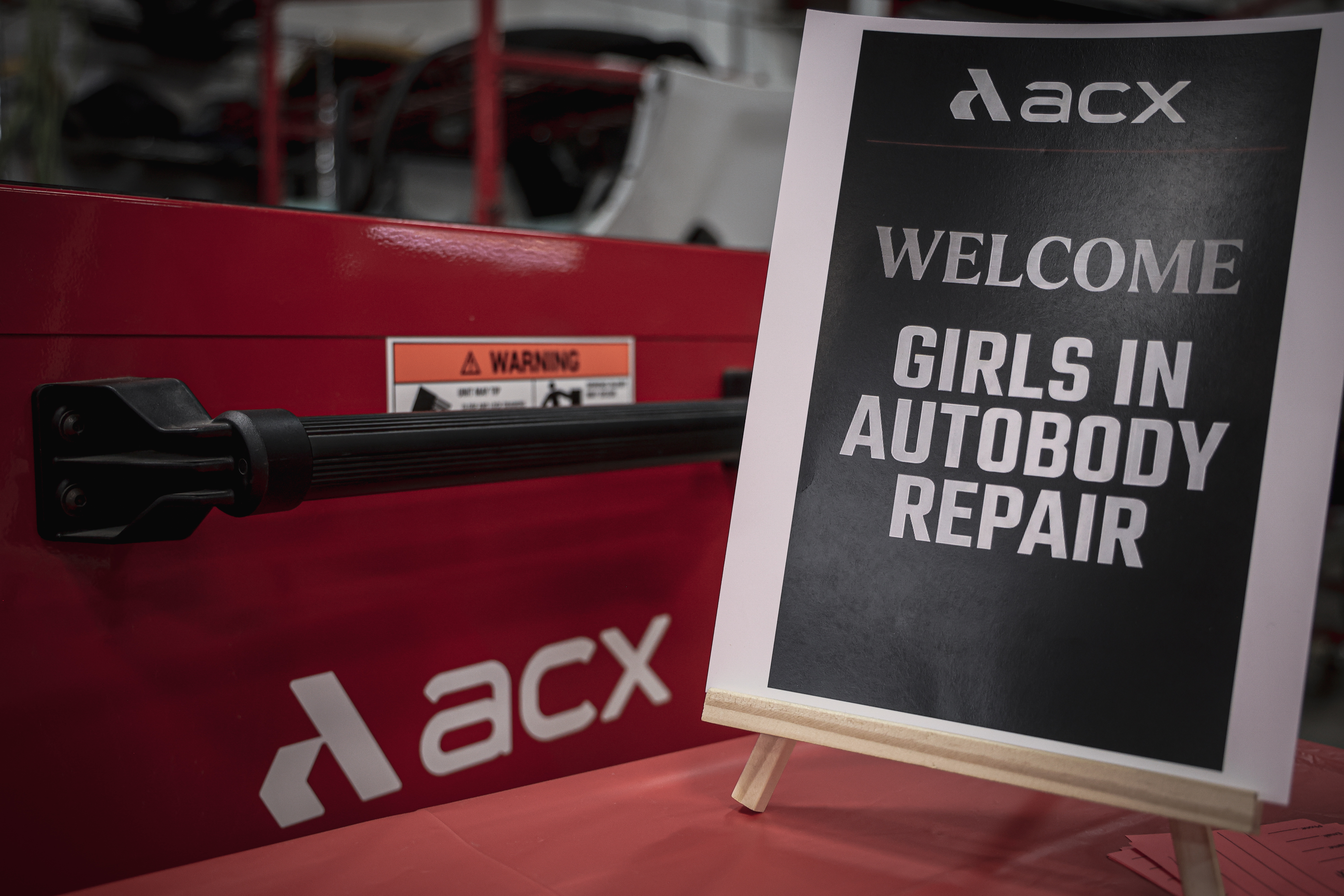 ACXS branded red equipment with welcome sign promoting girls in autobody repair program