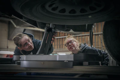 Two female automotive technicians inspecting underneath a vehicle during maintenance work