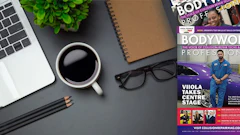 Workspace desk with laptop, coffee, notebook, glasses, and BodyWorx Professional magazine cover featuring Viola