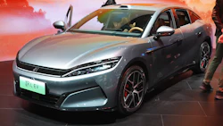Silver BYD electric sedan on display at automotive exhibition with dramatic orange sunset backdrop