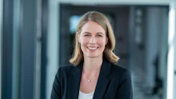 Professional woman with blonde hair smiling in modern office corridor wearing black blazer