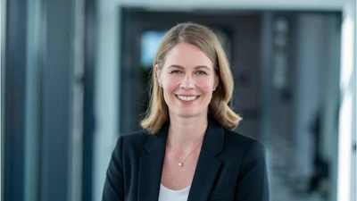 Professional woman with blonde hair smiling in modern office corridor wearing black blazer