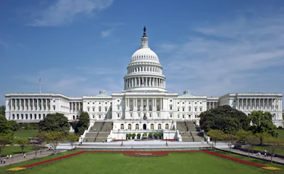 United States Capitol Building with white neoclassical dome, columned facade, and manicured gardens under blue sky