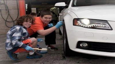 Two young people washing a white car's headlight in a garage
