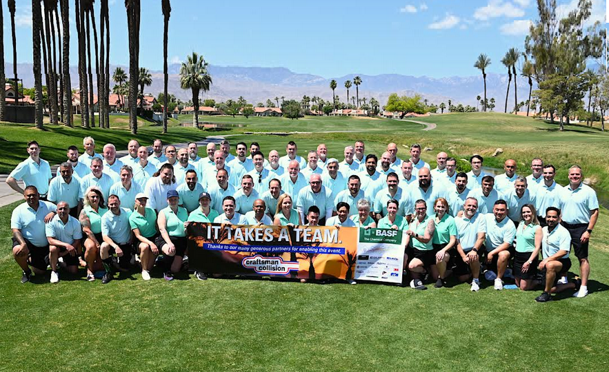 Large team group photo on golf course with 60+ people in light blue and green shirts holding charity banners