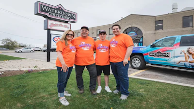 Four team members in orange shirts pose outside Waterdown Collision auto body shop with branded signage and service vehicle