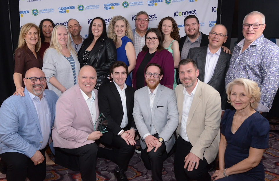 Group of 16 professionals posing at iConnect corporate event with branded backdrop