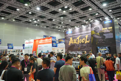 Crowded trade show exhibition floor with multiple vendor booths displaying automotive products and services
