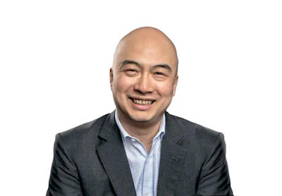 Professional headshot of a smiling Asian man in business attire against white background