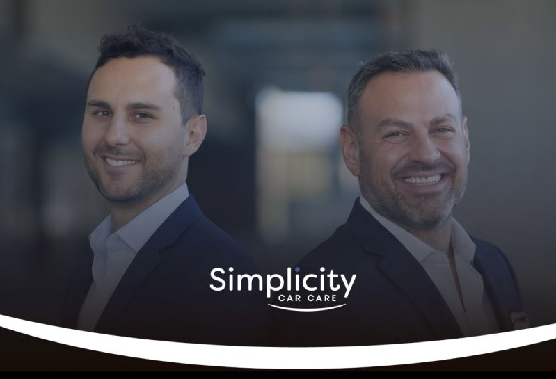 Two professional men in business attire smiling at camera with Simplicity Car Care logo overlay