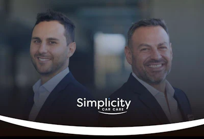 Two professional men in business attire smiling at camera with Simplicity Car Care logo overlay