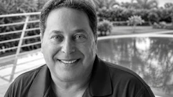 Professional black and white portrait of a smiling man outdoors with water and palm trees in background
