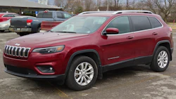 Red Jeep Cherokee SUV parked in lot with white alloy wheels and bare trees in background