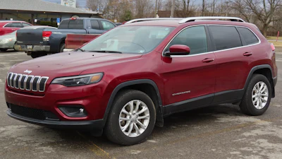Red Jeep Cherokee SUV parked in lot with white alloy wheels and bare trees in background