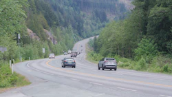 Mountain highway with vehicles traveling through forested valley with winding road