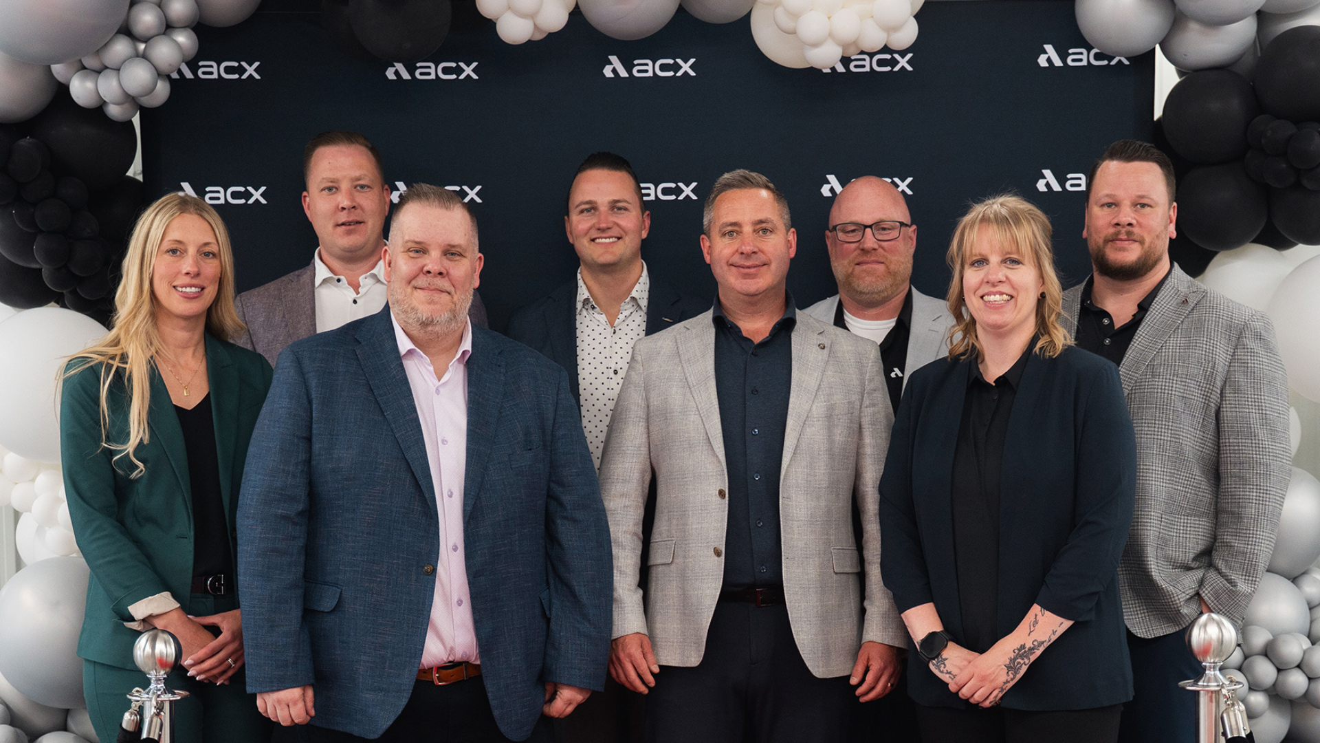 Nine business professionals posing together at an ACX corporate event with black and white balloon decorations