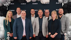 Nine business professionals posing together at an ACX corporate event with black and white balloon decorations
