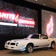 White Pontiac Firebird sports car displayed at indoor event venue with neon signage backdrop