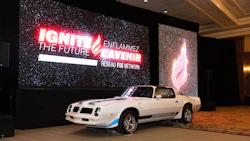 White Pontiac Firebird sports car displayed at indoor event venue with neon signage backdrop
