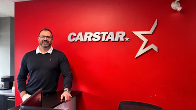 Professional man in dark sweater standing in front of red CARSTAR office wall with company logo and star symbol