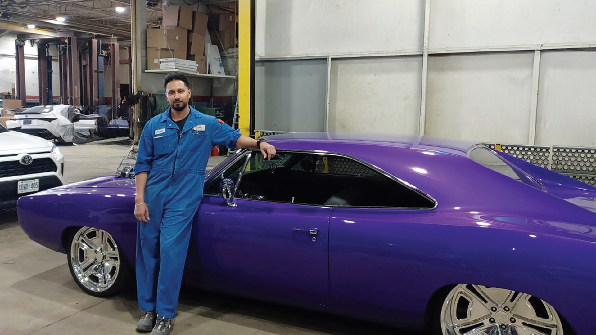 Mechanic in blue uniform standing beside purple custom car in workshop garage