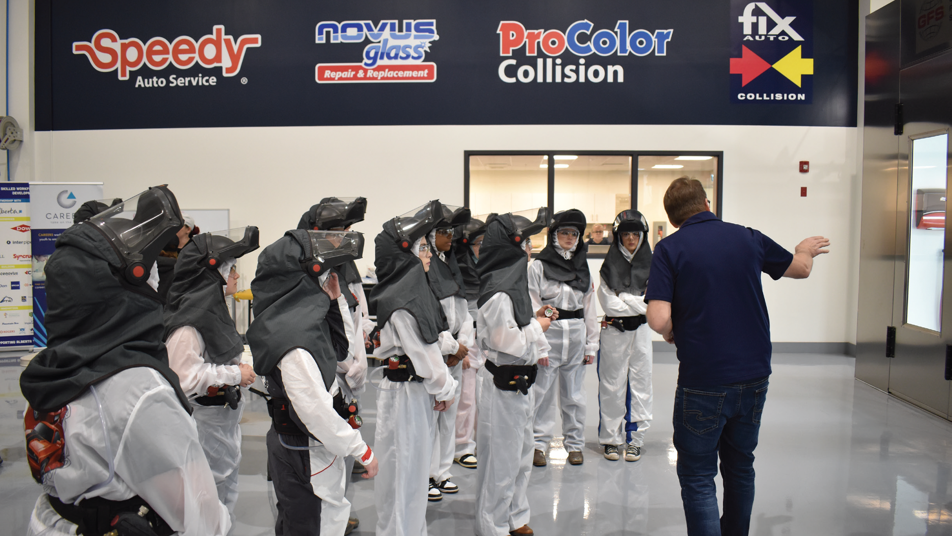 Group of people wearing protective gear and helmets during a training session at an auto service facility with branded signage overhead.