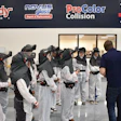 Group of people wearing protective gear and helmets during a training session at an auto service facility with branded signage overhead.