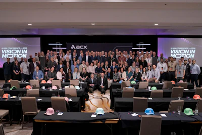 Large group photo from ACX Audio Conference with attendees standing on stage, colorful hard hats on tables, and ACX branding backdrop