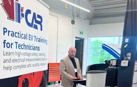 Instructor conducting EV training session in workshop with IFCAR signage and electrical equipment visible