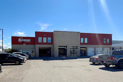 Contemporary automotive service facility with maroon and gray facade, multiple garage bays, and parking lot on sunny day