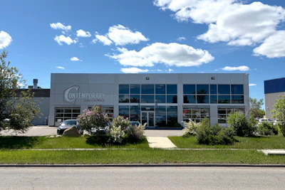 Contemporary business building with modern gray facade, large windows, and landscaping under blue sky with white clouds
